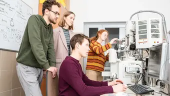 grupa młodych ludzi stoi przy komputerze